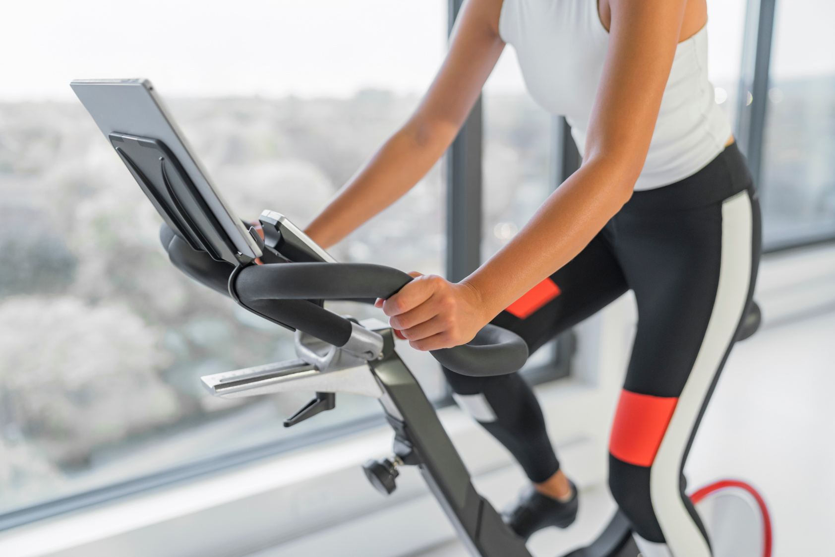 Exercise at Home on Spin Bicycle Fitness Workout with Screen. Woman Training on Stationary Bike Watching Online Video Class for Exercising Cardio.